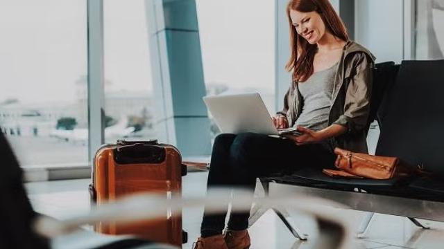 Woman working on a laptop sitting in an airport demonstrating the importance of business travel insurance for travel delays and cancellations.