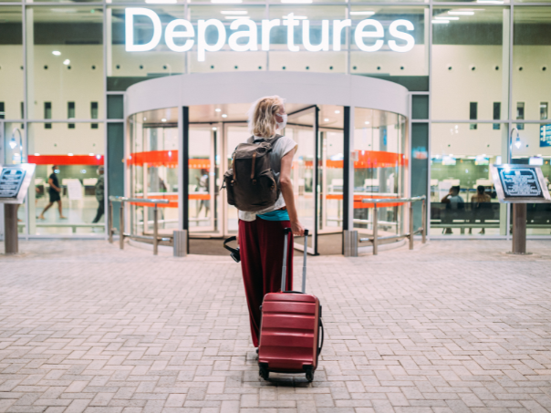 Blonde woman with suitcase outside departures terminal