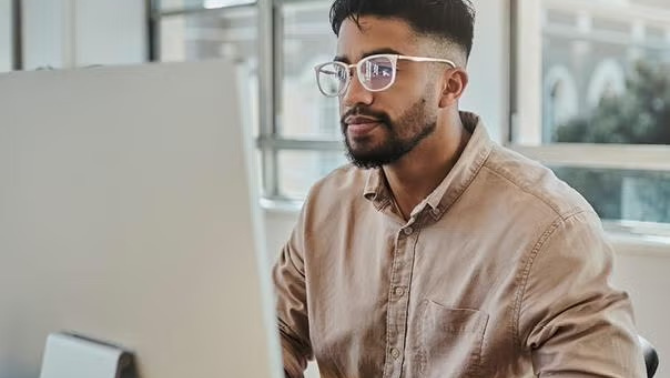 Man sitting in an office looking at a pc monitor demonstrating how Corporate Traveller's achievement of ISO 27001 certification, a globally recognised standard for information security management. 