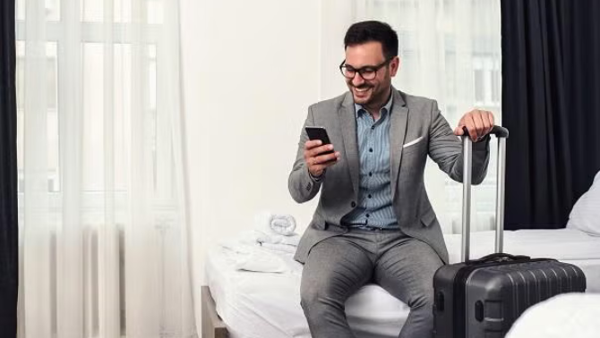 A smiling man sitting on a hotel bed demonstrating accommodation essentials for Kiwi corporate travellers.