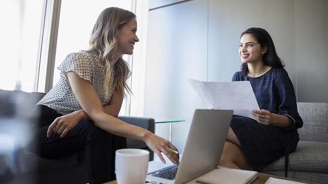 Two women in discussion looking at documents demonstrating the importance of business travel insurance for travel delays and cancellations.