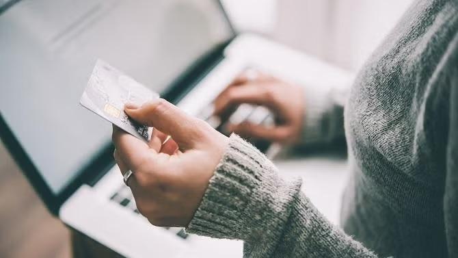 Woman holding credit card while working on the laptop demonstrating the importance of understanding credit card insurance. 