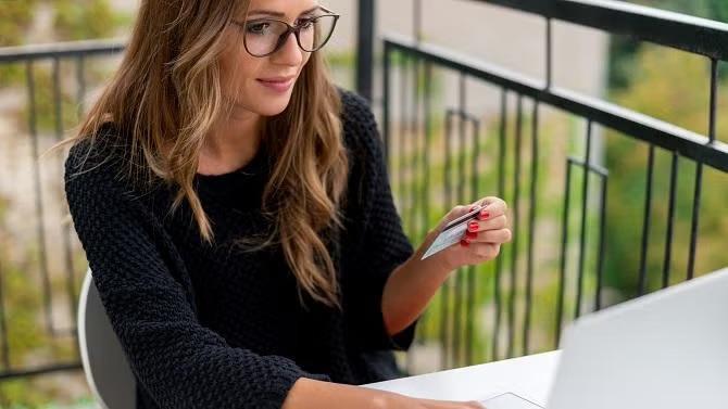 A woman holding credit card while working on the laptop demonstrating the importance of understanding credit card insurance. 