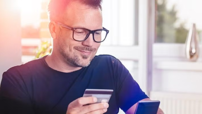 Man holding credit card and smartphone demonstrating the importance of understanding credit card insurance.