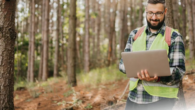 Man standing in the forest holding a laptop representing how together with Corporate Traveller, OfficeMax makes sure that travel is as sustainable as possible