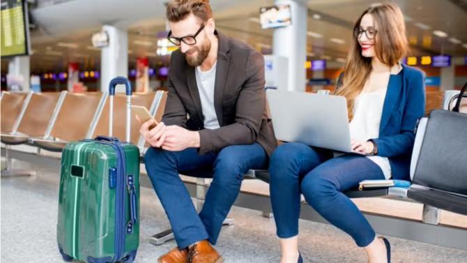 A man and woman sitting in an airport with a small suitcase demonstrating the benefits of packing light for business trips.