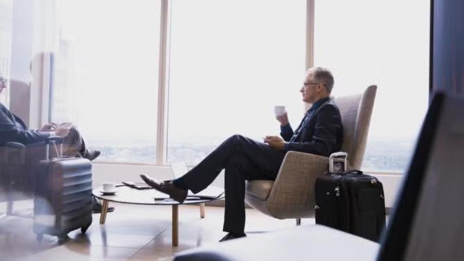 Man sitting in the business lounge enjoying a cup of coffee with a suitcase demonstrating the benefits of packing light for business trips. 