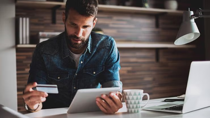 Man holding a credit card and tablet demonstrating tactics for beating travel cost blowout.