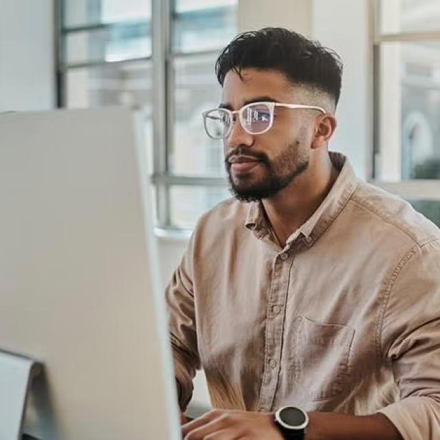 Man sitting in an office looking at a pc monitor demonstrating how Corporate Traveller's achievement of ISO 27001 certification, a globally recognised standard for information security management. 