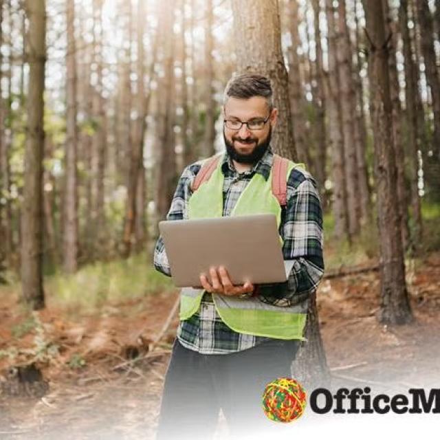 Man standing in the forest holding a laptop representing how together with Corporate Traveller, OfficeMax makes sure that travel is as sustainable as possible.